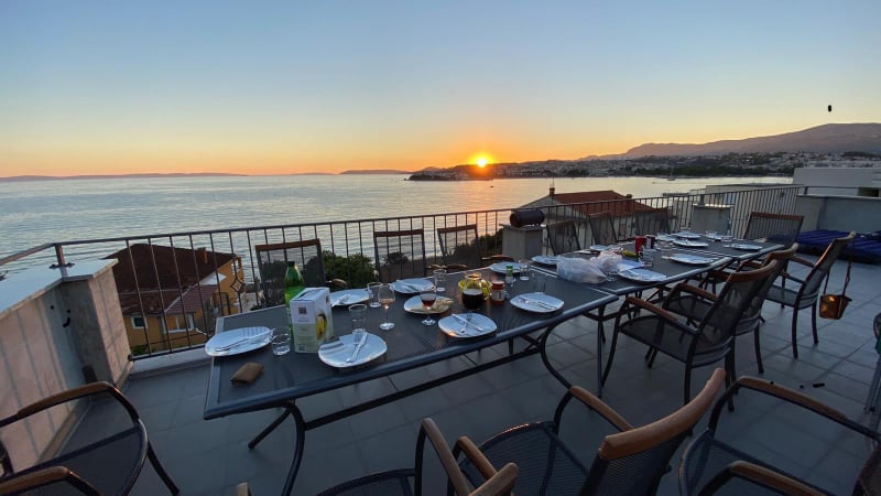 Terrasse mit Meerblick, ausgestattet mit Grill, Dusche, Liegestühlen, Tischen, Stühlen und Sonnenschirm.