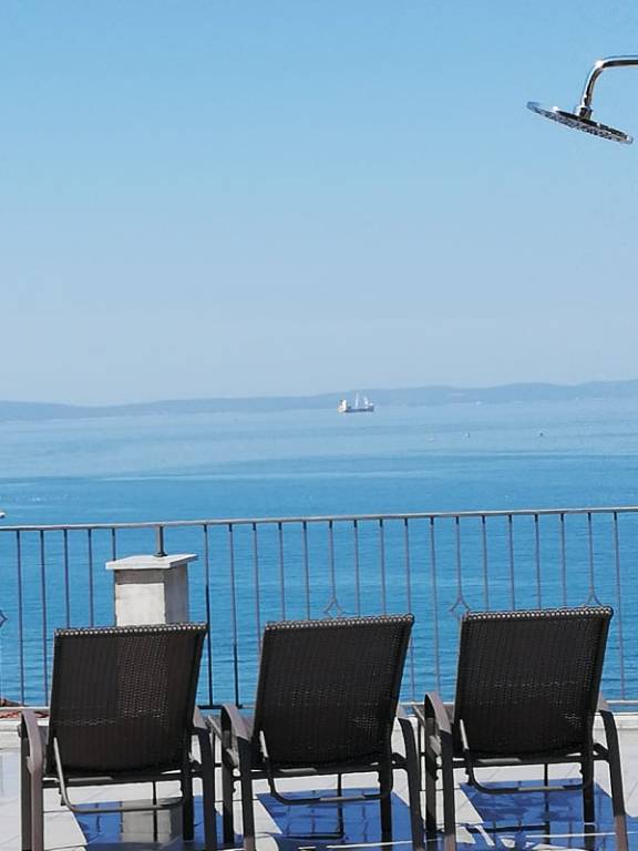 Terrasse mit Meerblick, ausgestattet mit Grill, Dusche, Liegestühlen, Tischen, Stühlen und Sonnenschirm.