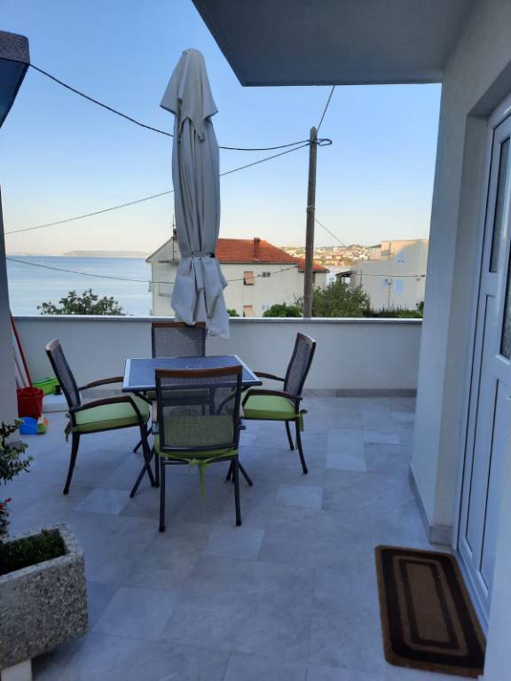 Terrasse mit Meerblick, ausgestattet mit Grill, Dusche, Tischen, Stühlen und Sonnenschirm.