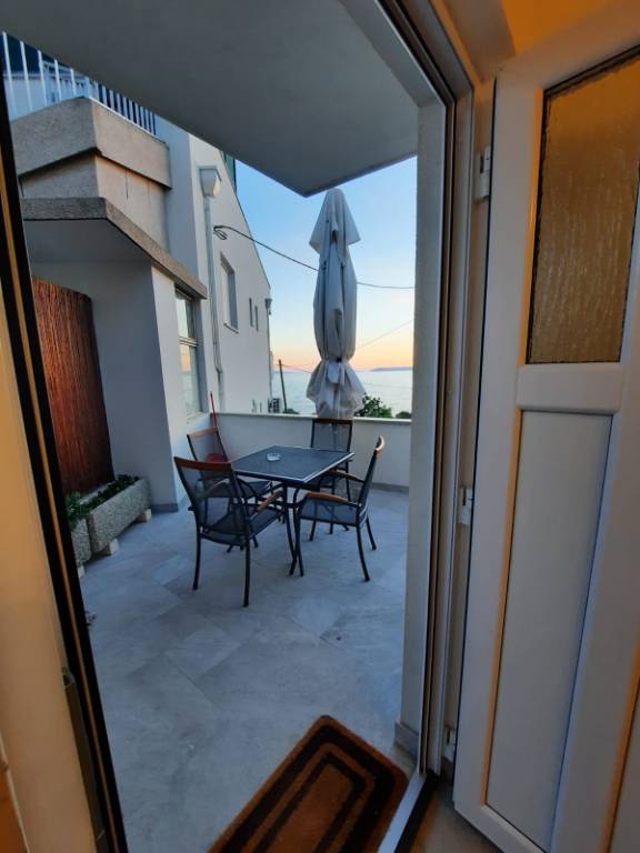 Terrasse mit Meerblick, ausgestattet mit Grill, Dusche, Tischen, Stühlen und Sonnenschirm.