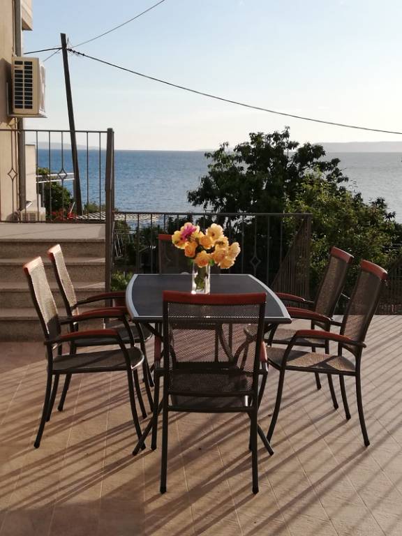 Terrasse mit Meerblick, ausgestattet mit Grill, Dusche, Liegestühlen, Tischen, Stühlen und Sonnenschirm.