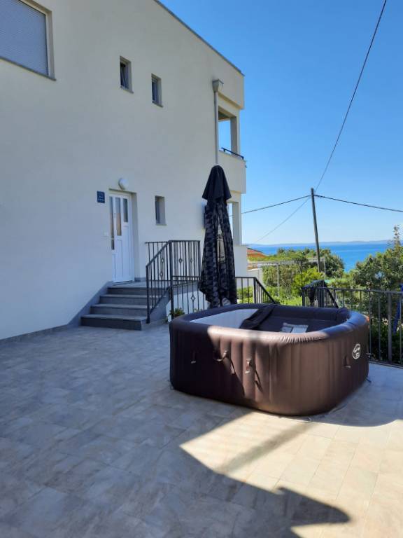 Terrasse mit Meerblick, ausgestattet mit Grill, Dusche, Liegestühlen, Tischen, Stühlen und Sonnenschirm.